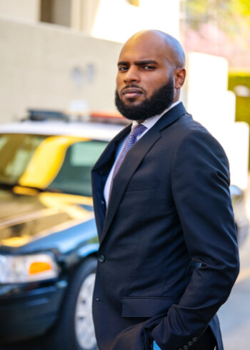 Eric Adams standing with hands in his pockets on a street in front of a cop car